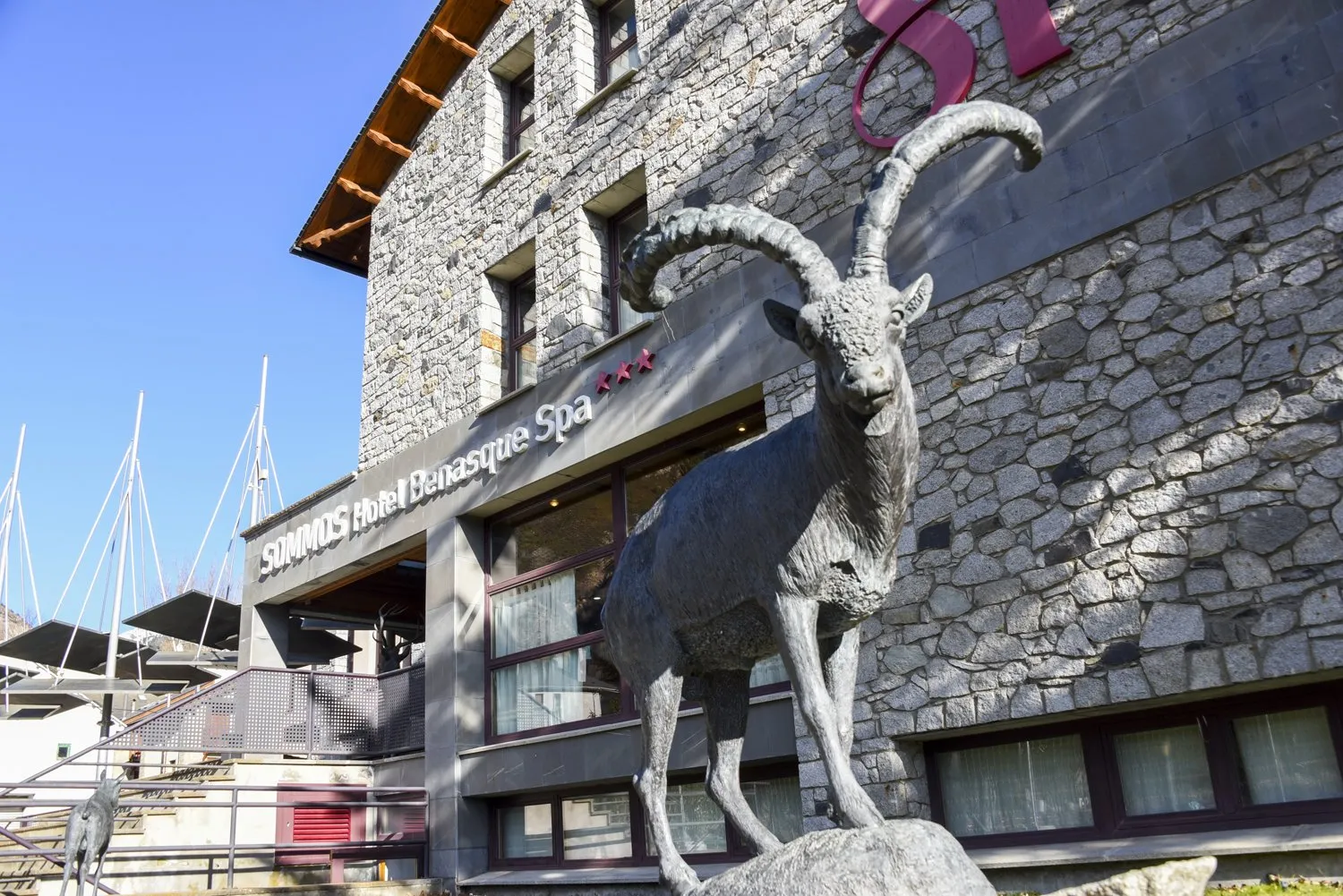 Entrada del SOMMOS Hotel Benasque Spa, con una escultura de cabra montesa en primer plano y la fachada de piedra del hotel