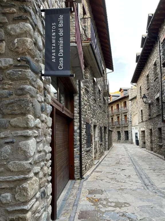 Cartel de Apartamentos Casa Damián del Baile colgado en una fachada de piedra, en una calle empedrada del casco antiguo de Benasque