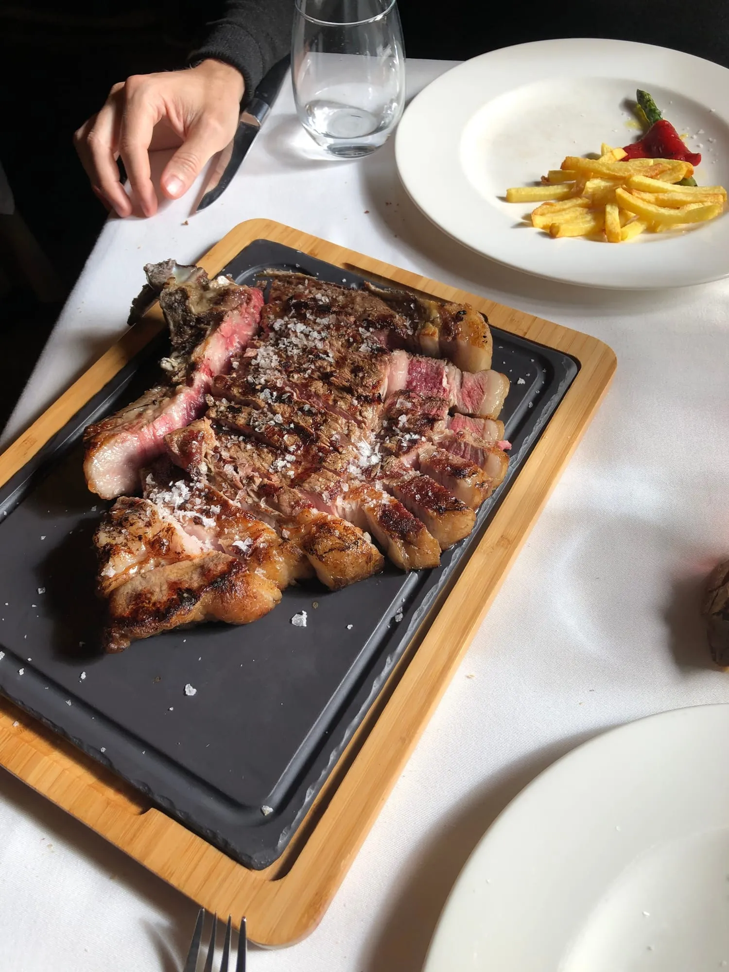 Chuletón a la brasa servido sobre tabla de pizarra, con patatas y pimiento, en un restaurante del valle