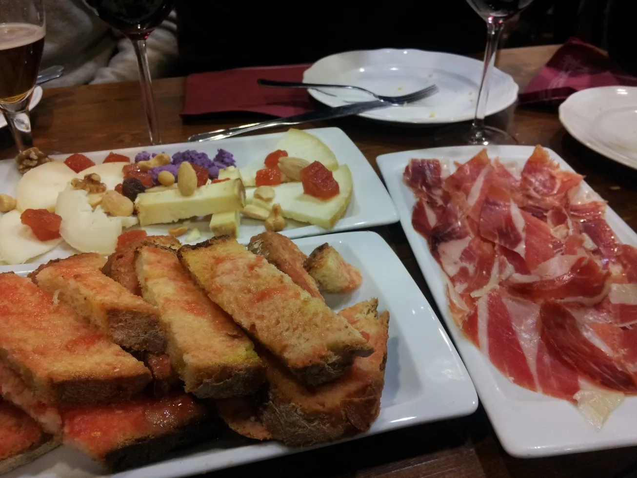 Tabla de tapas en El Veedor de Viandas: jamón ibérico, quesos con frutos secos y pan con tomate, con copas de vino