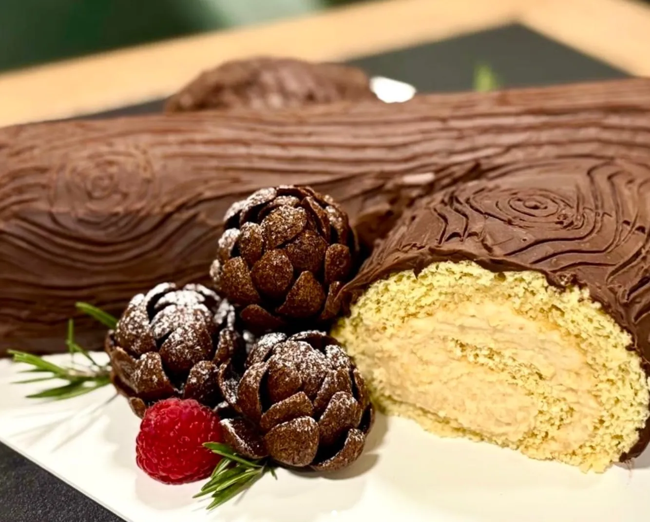Tronco de chocolate de Flor de Nieve con piñas de chocolate espolvoreadas de azúcar, una frambuesa y romero