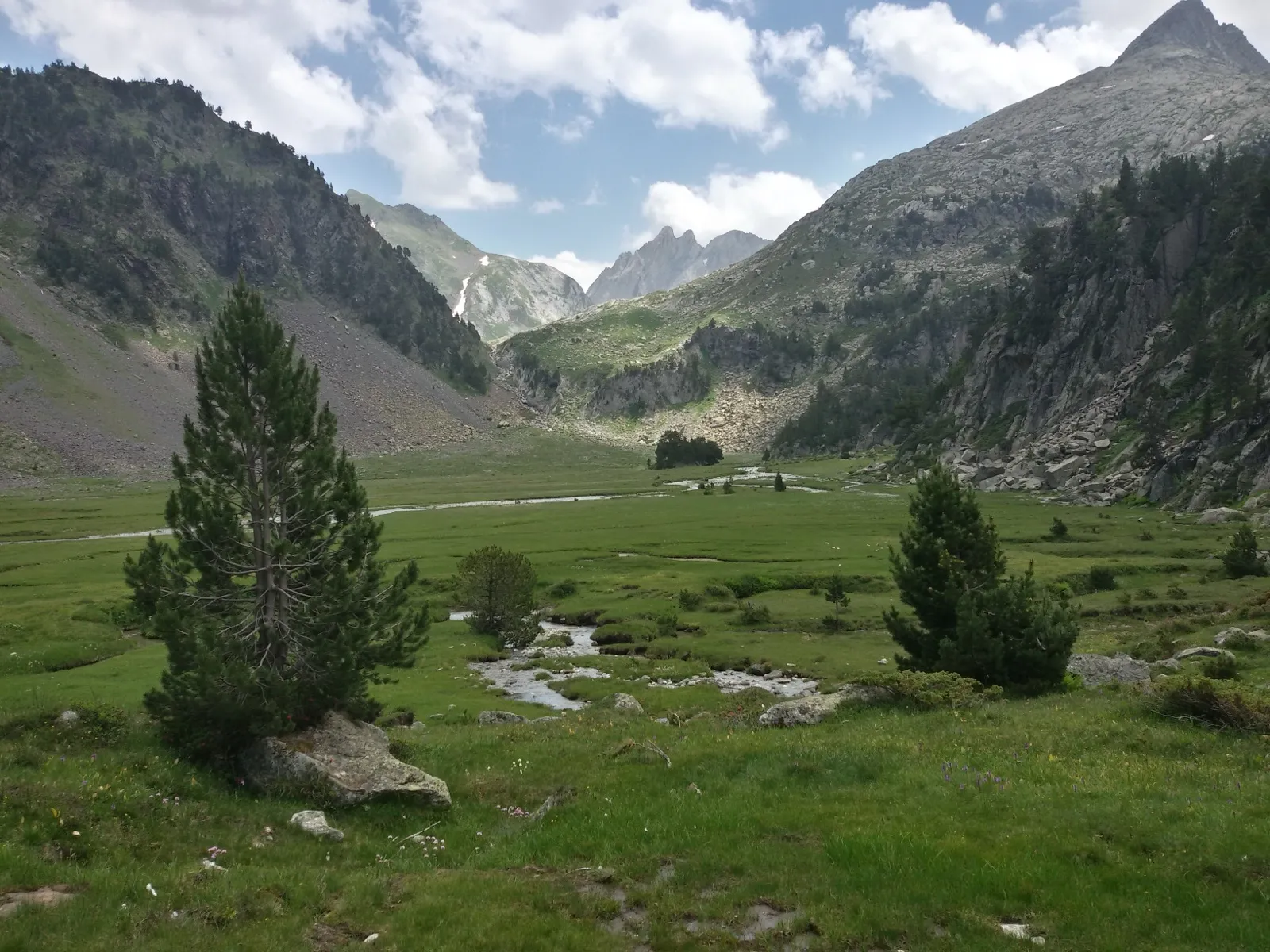 El Plan d'Estan, la pradera llana por la que serpentea el agua del deshielo, con las cimas del macizo de la Maladeta al fondo