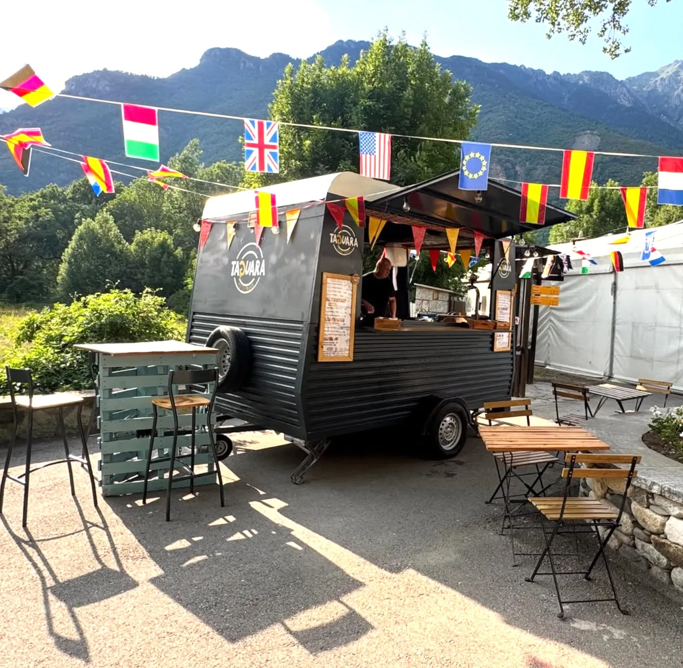 El foodtruck La Taguara, negro con el rótulo dorado, en una explanada con banderines, mesas y montañas al fondo